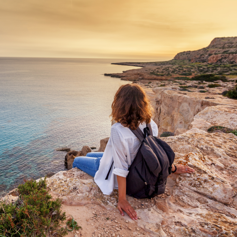 Eine stilvolle junge Reisende betrachtet einen wundersch&ouml;nen Sonnenuntergang auf den Felsen am Strand &ndash; Zypern
